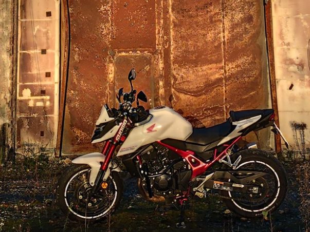 Ein weiß-rotes Motorrad steht vor einer rostigen Metallwand.