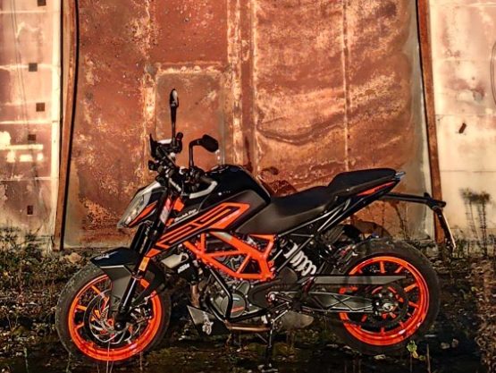 Schwarzes Motorrad mit orangefarbenen Akzenten vor einer rostigen Wand.
